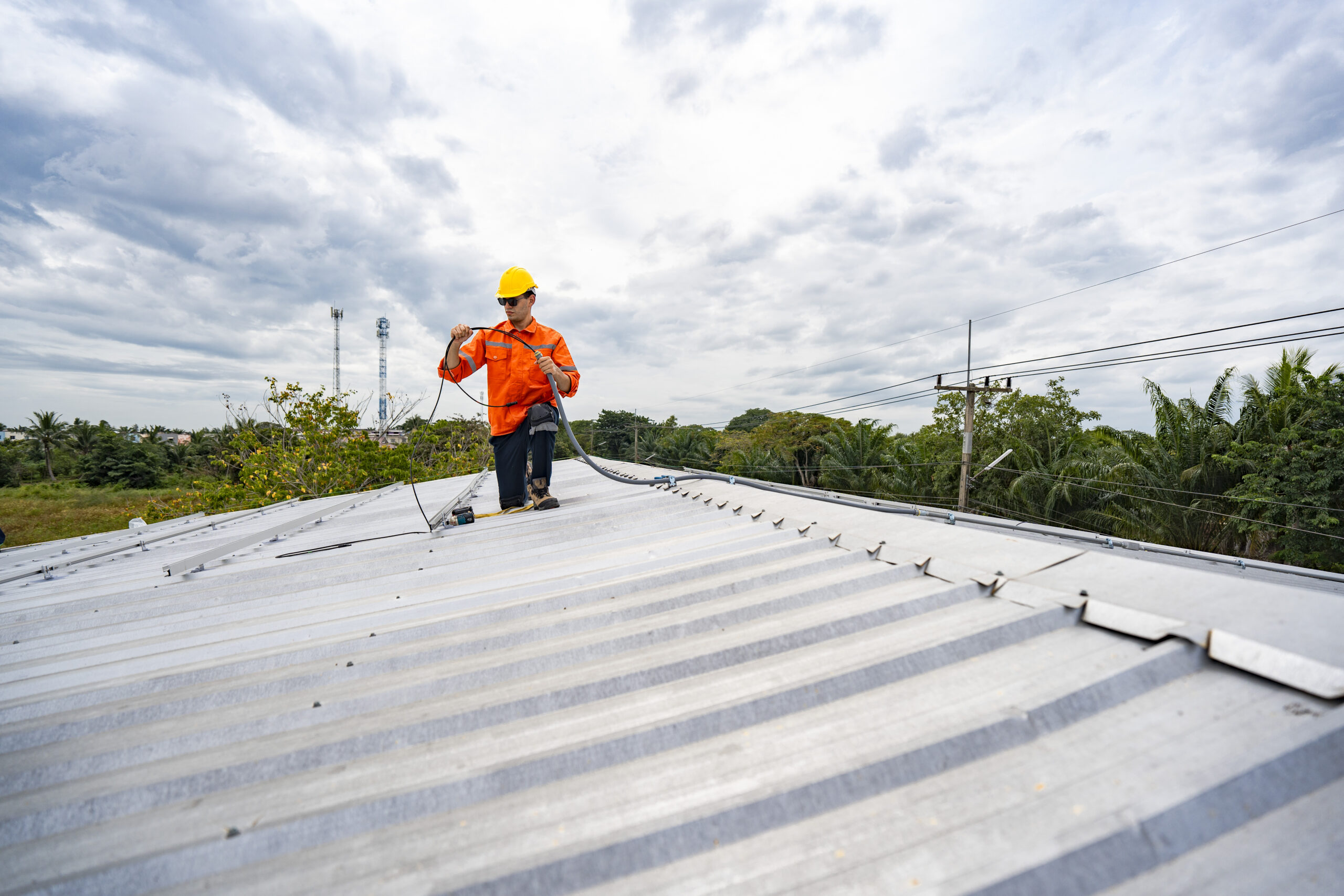 Technician in safety uniform and helmet kneeling on a rooftop, using a drill for precise installation work. A scene highlighting safety, professionalism, and technical expertise in construction.