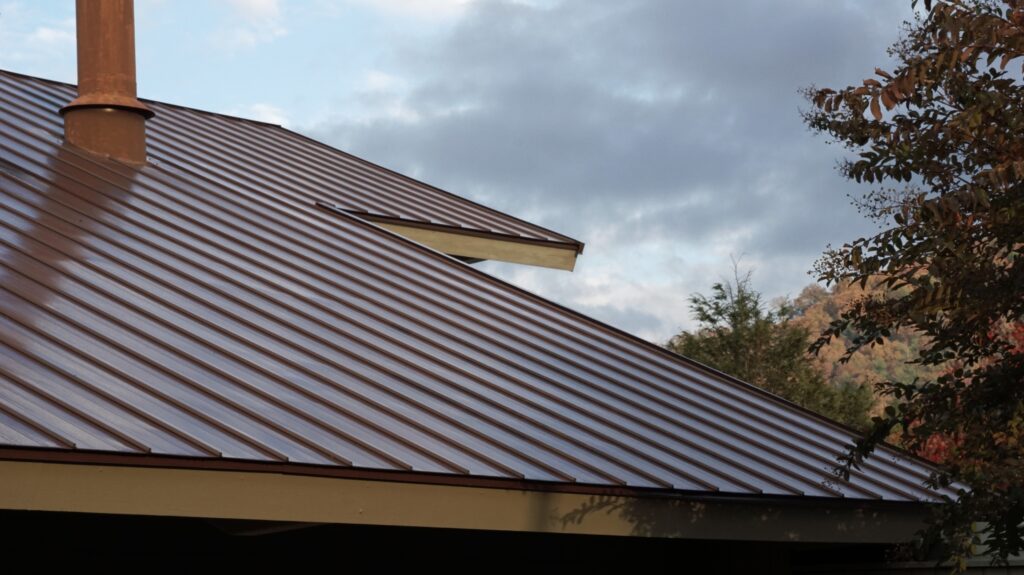 Commercial standing seam metal roof on a building in the Hudson Valley with a chimney, surrounded by trees and rolling hills under a cloudy sky