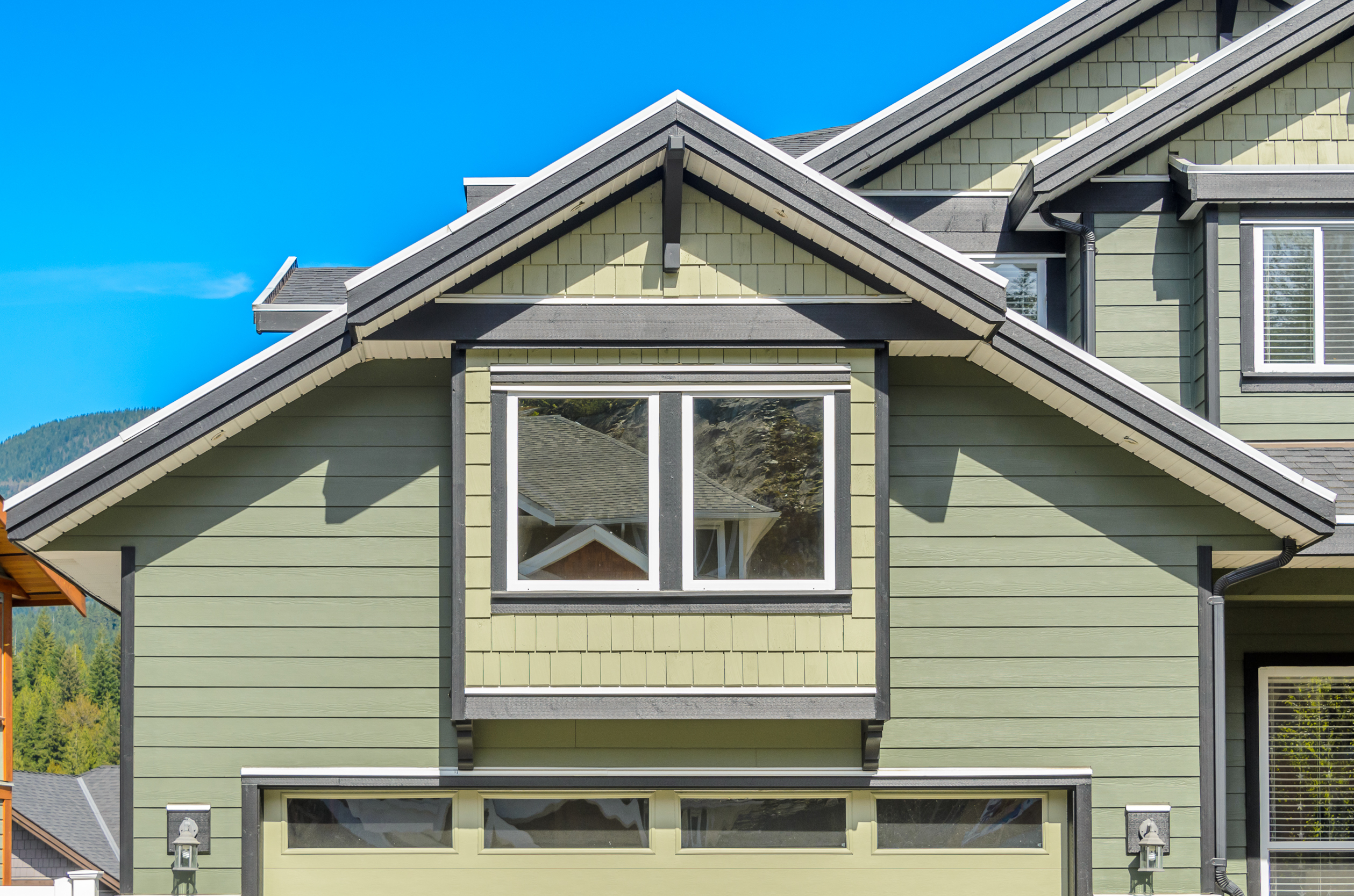 Fiber cement siding on a modern home with green lap siding, white trim, and a gabled roof under a clear blue sky