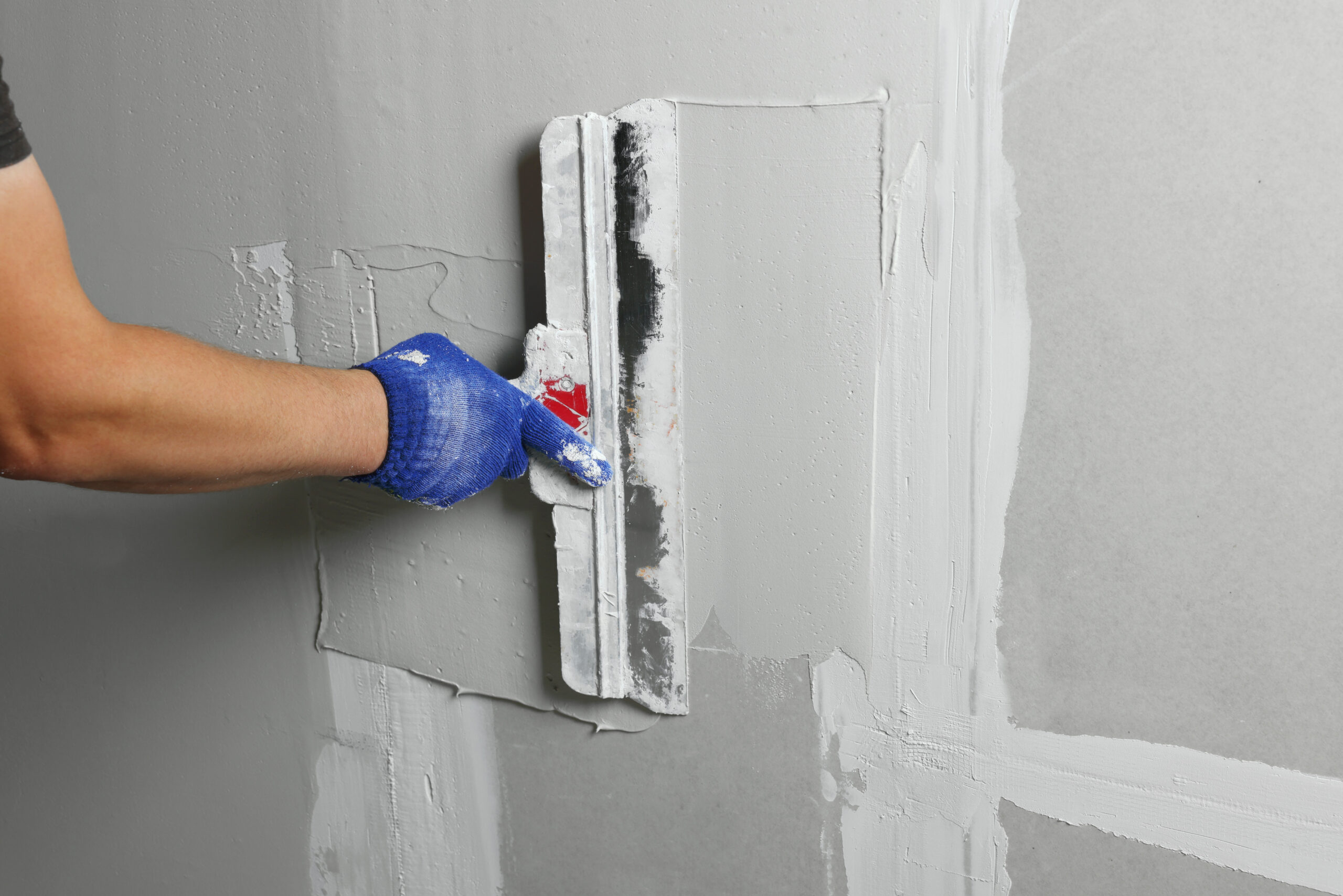 Professional worker plastering wall with putty knife, closeup
